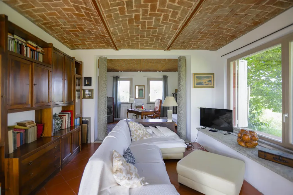 Rustic dream home in Italy – 3,000 m² surrounded by greenery with panoramic views, living room with sofa, bookcase and brick ceiling.