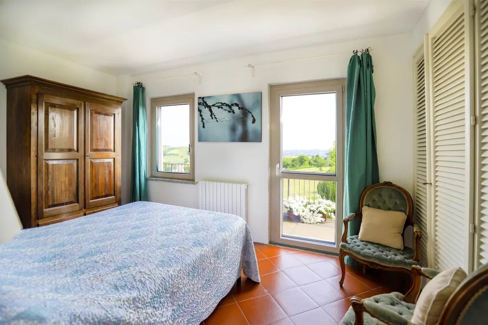 Rustic dream home in Italy – 3,000 m² surrounded by greenery with panoramic views, bedroom with balcony and hillside view.