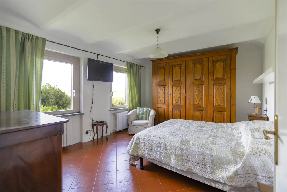 Rustic dream home in Italy – 3,000 m² surrounded by greenery with panoramic views, bedroom with large wooden wardrobe and TV.