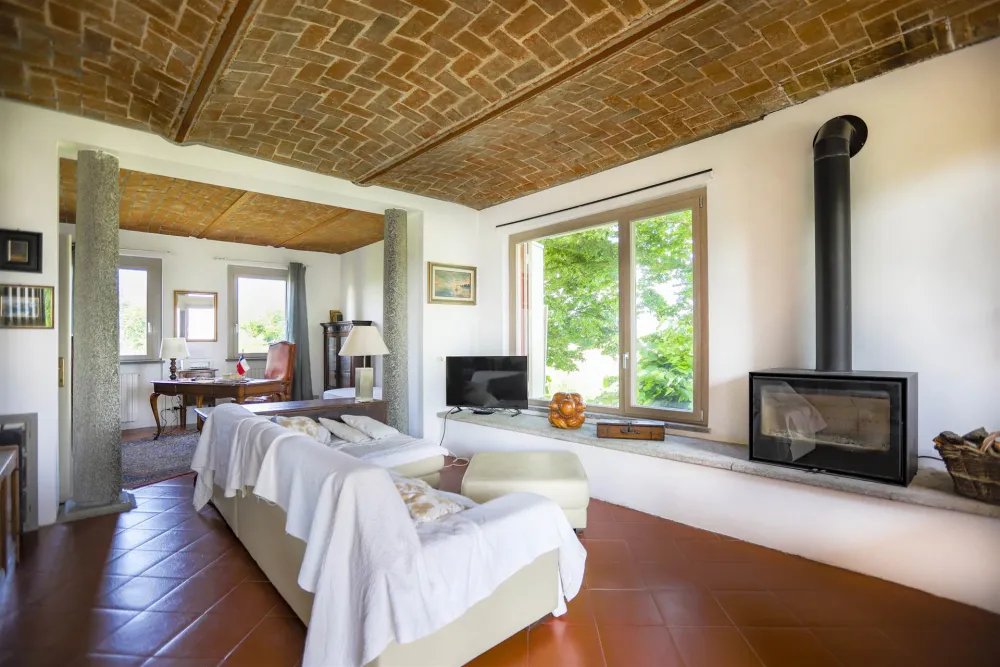 Rustic dream home in Italy – 3,000 m² surrounded by greenery with panoramic views, living room with fireplace, sofa and brick ceiling.