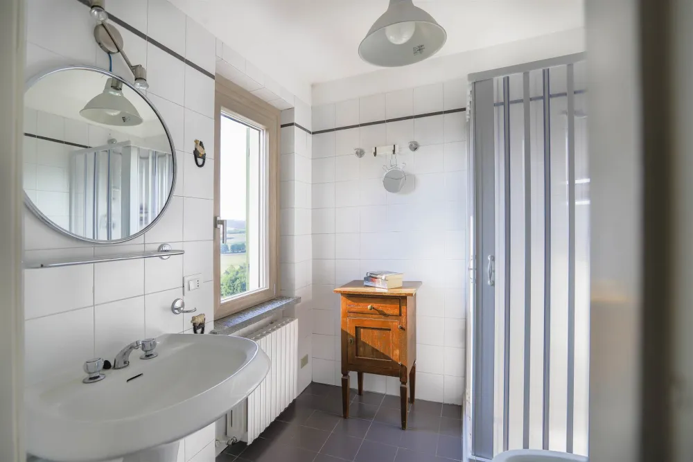 Rustic dream home in Italy – 3,000 m² surrounded by greenery with panoramic views, bathroom with shower, round mirror and window.
