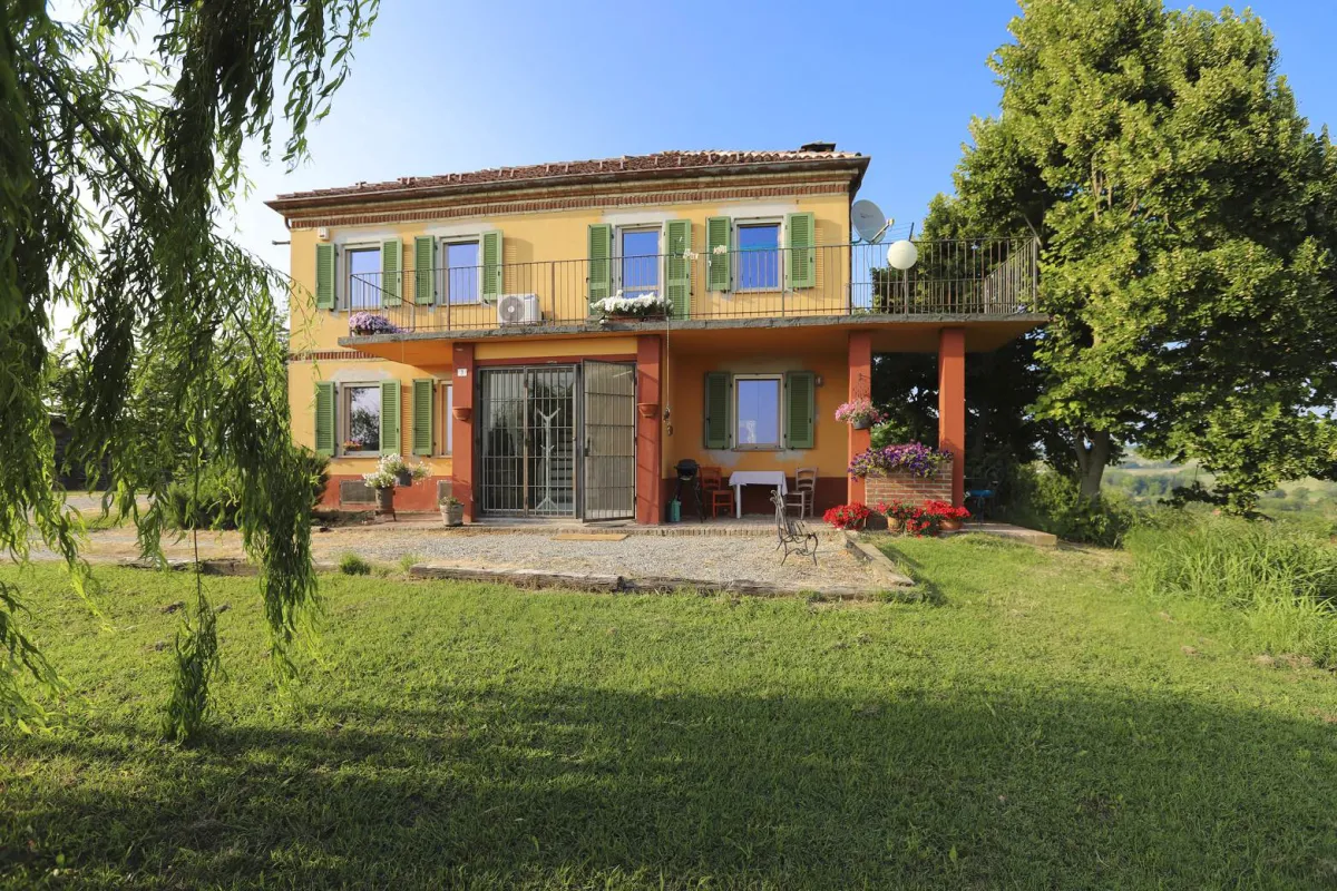 Rustic dream home in Italy – 3,000 m² surrounded by greenery with panoramic views, front view of the house with balcony and flowers.