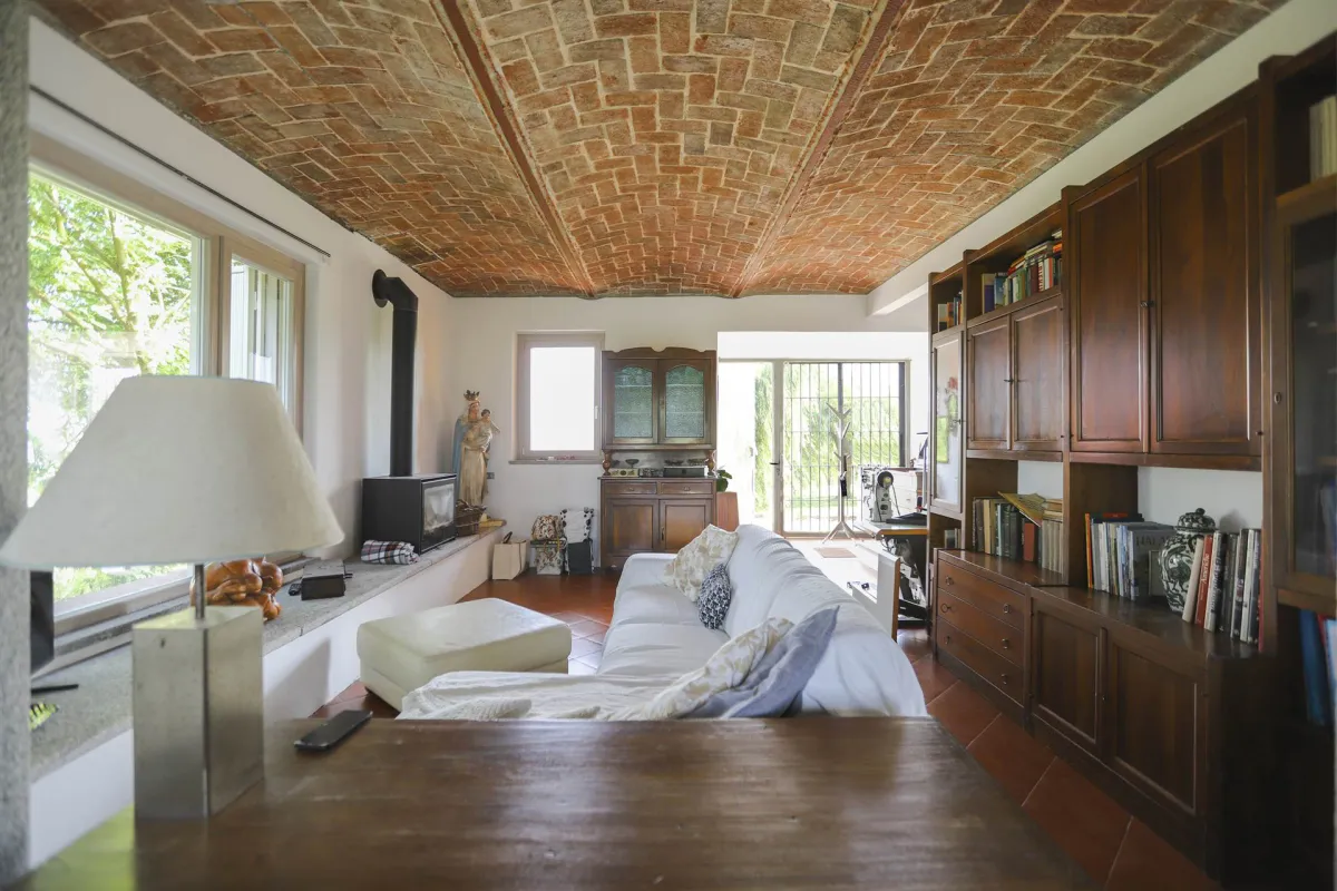 Rustic dream home in Italy – 3,000 m² surrounded by greenery with panoramic views, living room with sofa, bookcase and fireplace.